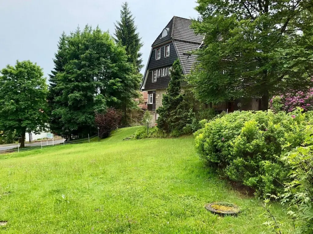 Hintergrundbild eines Hauses mit schwarzer Fassade, umgeben von grünen Bäumen und einem gepflegten Garten.