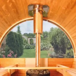 Innenansicht einer Sauna mit einem Kupferofen, Blick auf einen blühenden Garten durch ein großes Rundfenster.