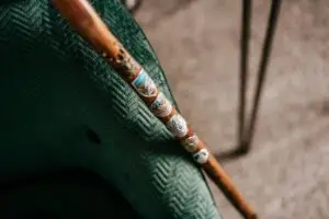 Detailaufnahme eines Gehstocks mit bunten Emblemen auf einem grünen gepolsterten Stuhl im Hintergrund.