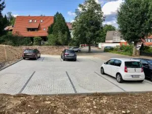 Parkplatz mit vier Autos auf neu gepflasterter Fläche, im Hintergrund Wohnhäuser und eine Baustelle.