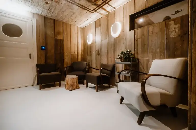 Gemütliche Sitzecke mit zwei dunklen und einem hellen Sessel, rundem Holztisch und Pflanzen vor einer Holzwand.
