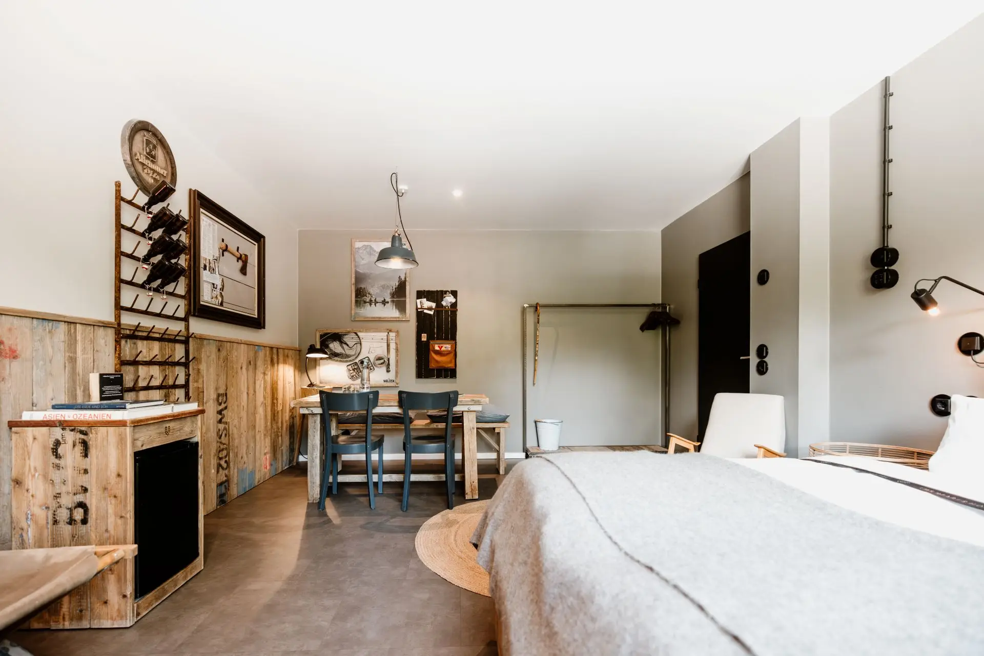 Helles Zimmer mit einem Bett, Tisch, Stühlen und Stauraum. Holz- und Grautöne prägen das moderne Design.