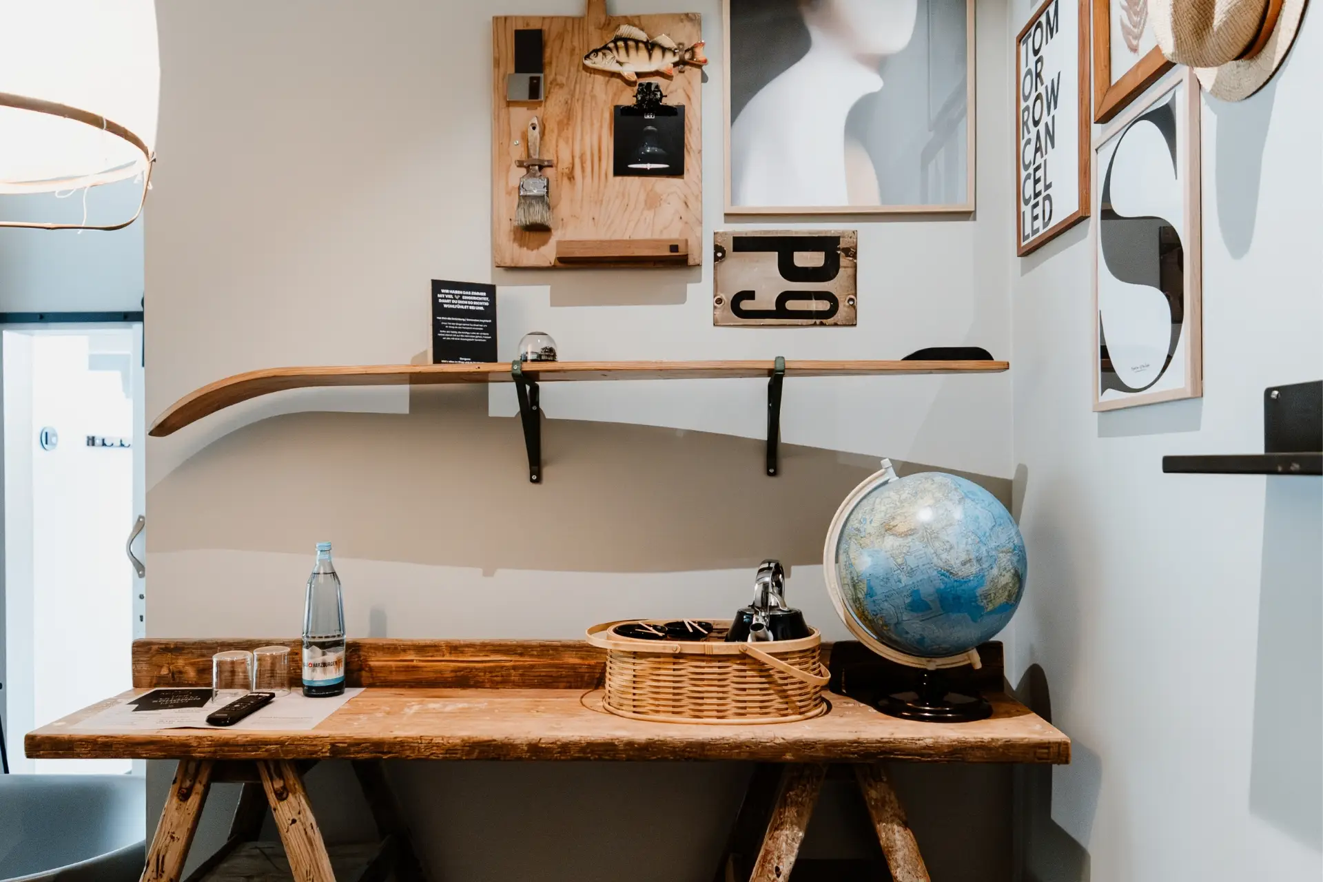 Holztisch mit Wasserflasche, Gläsern und Weltkugel; an der Wand Regale mit Dekoration und Kunstwerken.