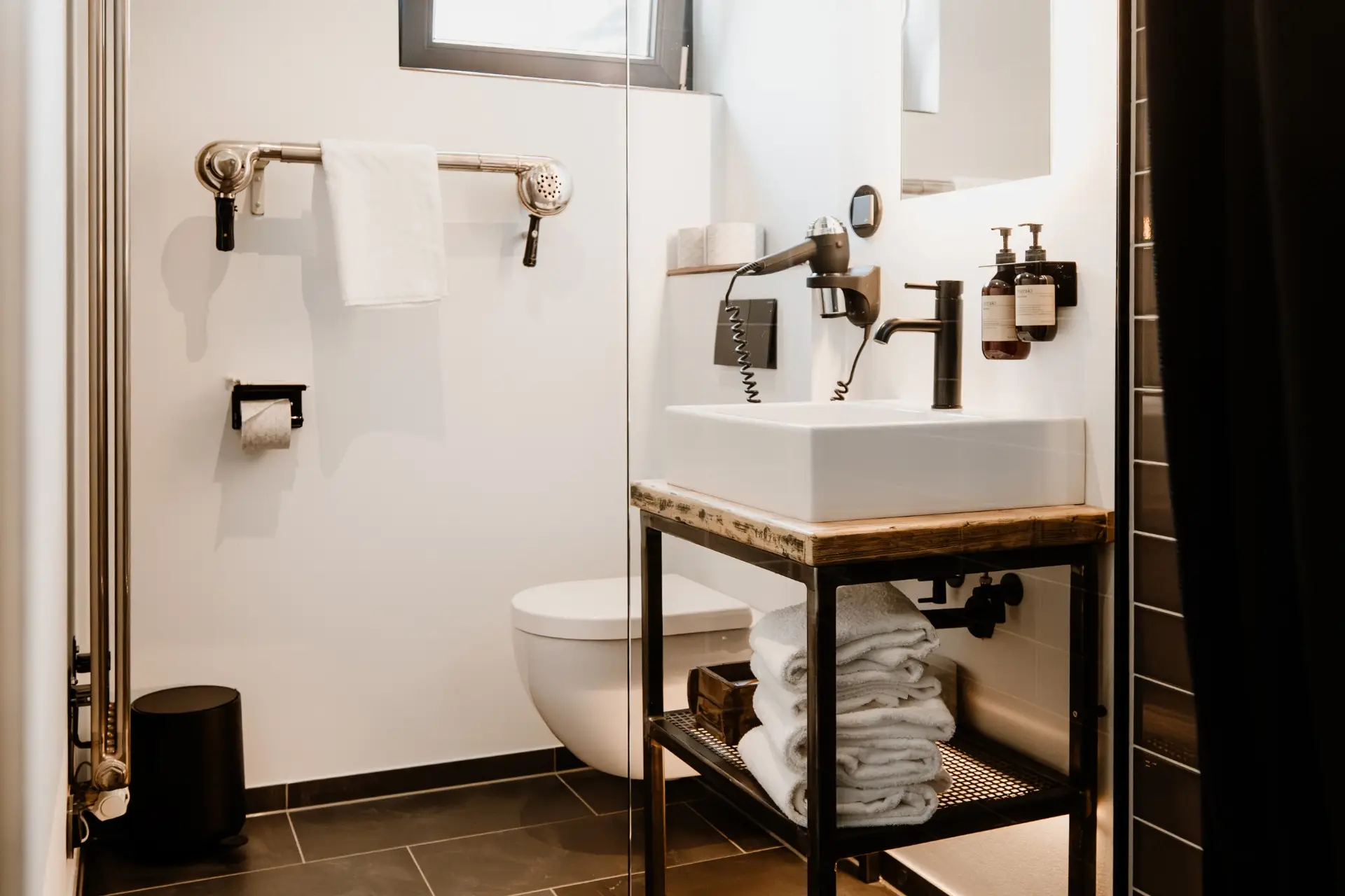 Modernes Badezimmer mit Toilette, Waschbecken, Handtuchhalter und Handtrockner. Sauber und gut organisiert.