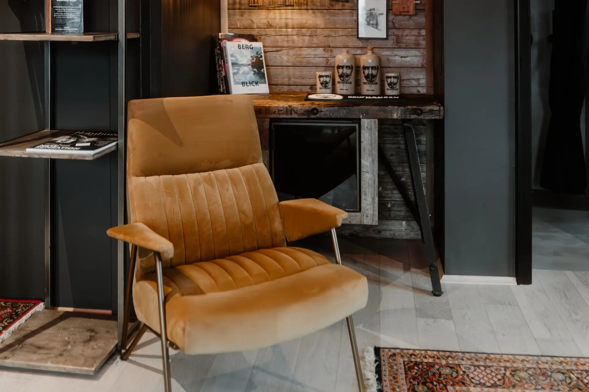 Beige Sessel steht vor einem Regal mit Büchern, Holztheke im Hintergrund mit Dekoobjekten und Fotos an der Wand.
