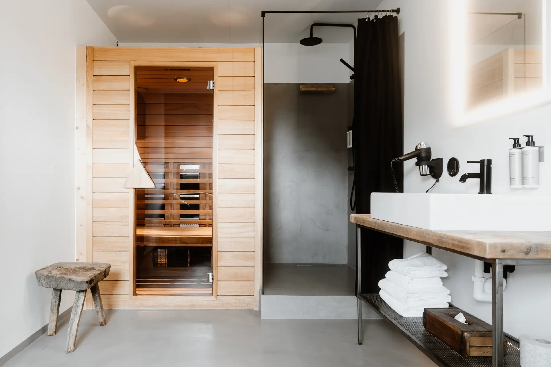 Moderne Sauna mit holzverkleideter Tür, angrenzender Dusche und Waschbecken. Handtücher und Pflegeprodukte sind sichtbar.