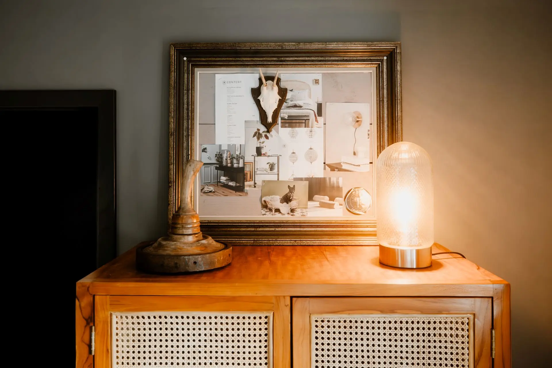 Holzschrank mit gerahmtem Kunstwerk und Beleuchtung; das Kunstwerk zeigt Möbel und Accessoires in stilvollem Arrangement.