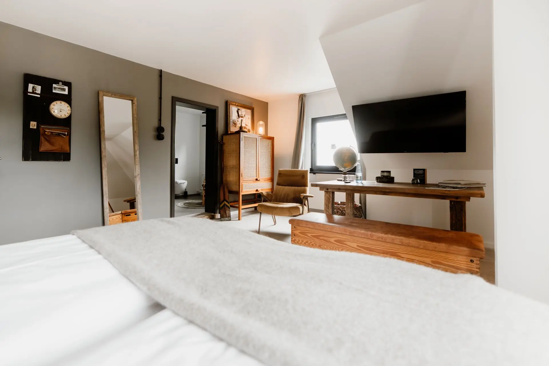Modernes Schlafzimmer mit Doppelbett, Fernseher, Schreibtisch, Stuhl und großen Fenstern. Auf dem Tisch steht eine Weltkugel.
