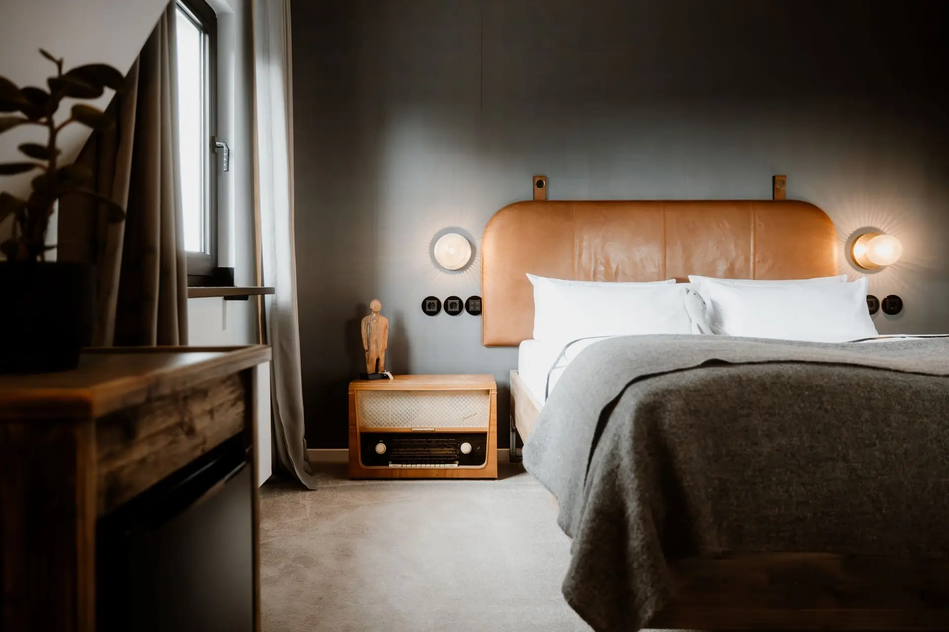 Moderner Schlafzimmerbereich mit einem großen Bett, Holzregal, Vintage-Radiogerät und Fenster mit Vorhängen.
