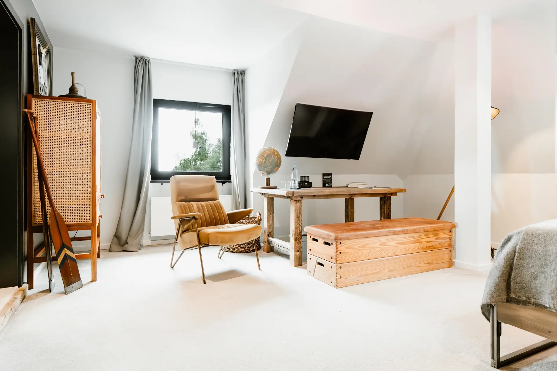Heller Raum mit Holzmöbeln, einer beigen Lesecouch und einem Fernseher. Fenster mit Aussicht auf Bäume, Teppichboden.