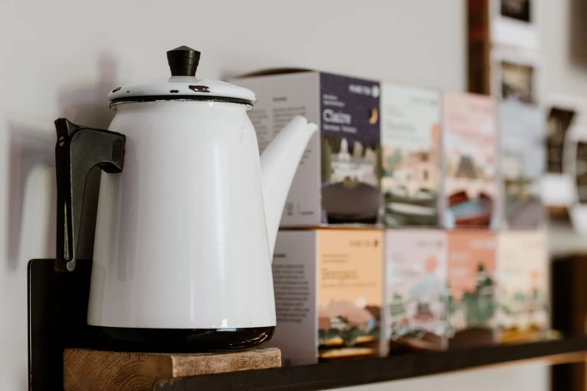 Weißer Kaffeekocher steht auf einem Regal vor einer Auswahl von Teeverpackungen.