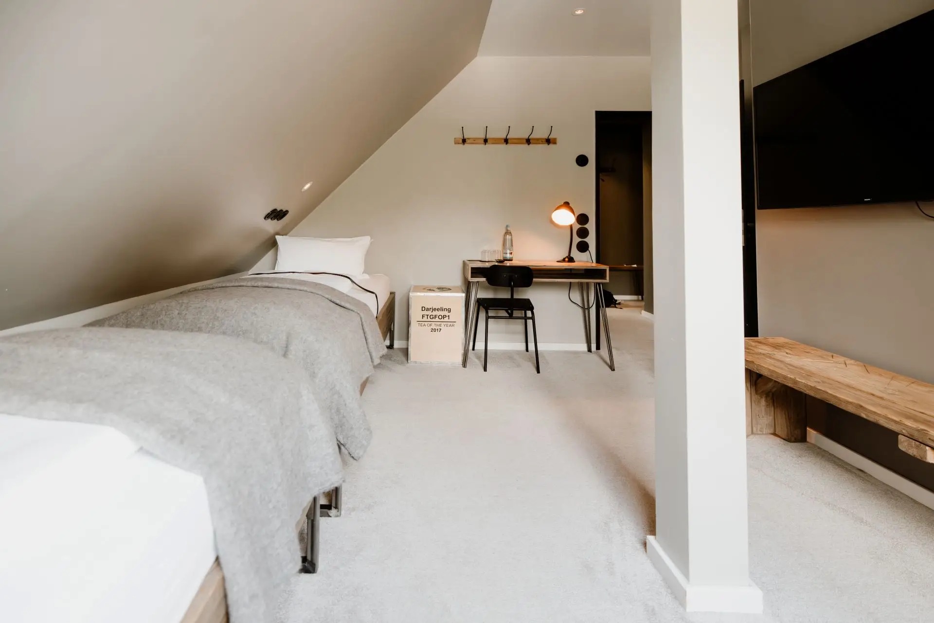 Schlichtes Schlafzimmer unter dem Dach mit zwei Betten, Schreibtisch, Stuhl und Fernseher. Helle, moderne Einrichtung.