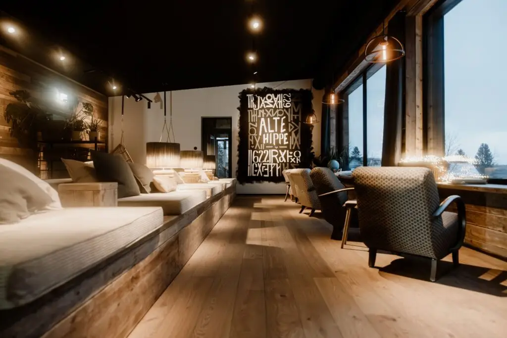 Gemütlicher Innenraum mit Holz-Elementen, Sitzmöglichkeiten und Kunstwerk an der Wand, große Fenster bieten Ausblick ins Freie.