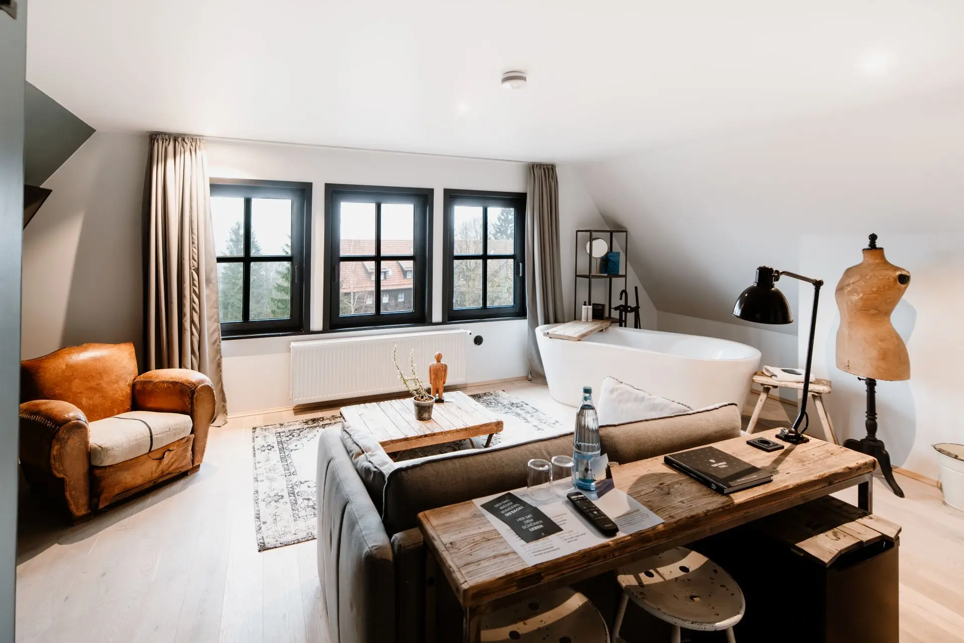 Helles, modernes Zimmer mit Sitzbereich, freistehender Badewanne, Arbeitsbereich und großen Fenstern mit Blick ins Freie.