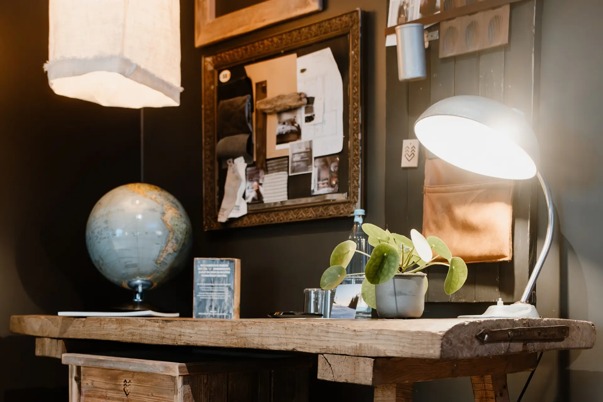 Ein Holztisch mit einer Lampe, einer Pflanze, einem Globus und verschiedenen Notizen an der Wand in einem stilvollen Raum.