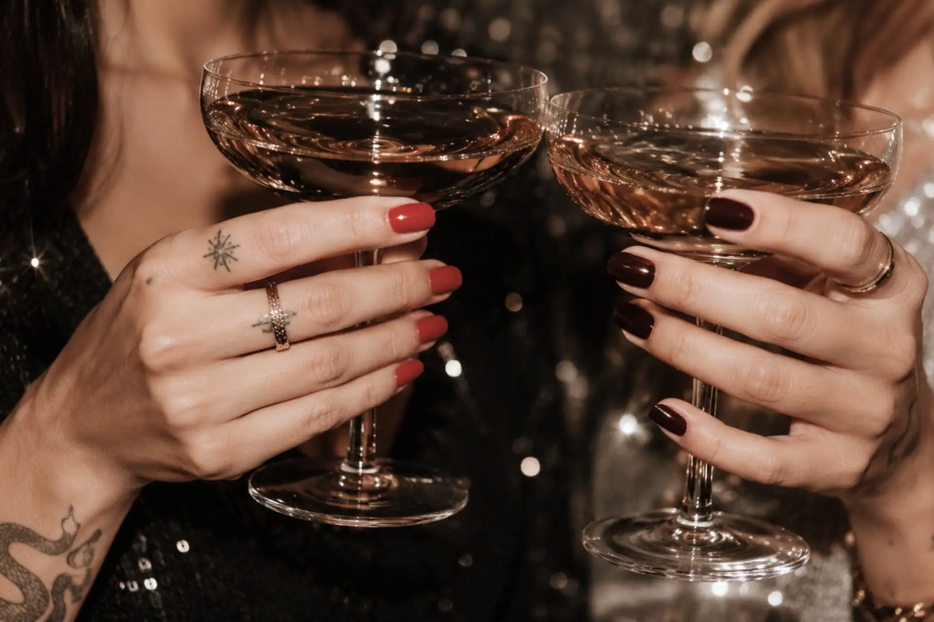 Zwei Frauen halten Sektgläser mit Rosé in einer festlichen Umgebung. Eine trägt rote und die andere dunkelrote Fingernägel.
