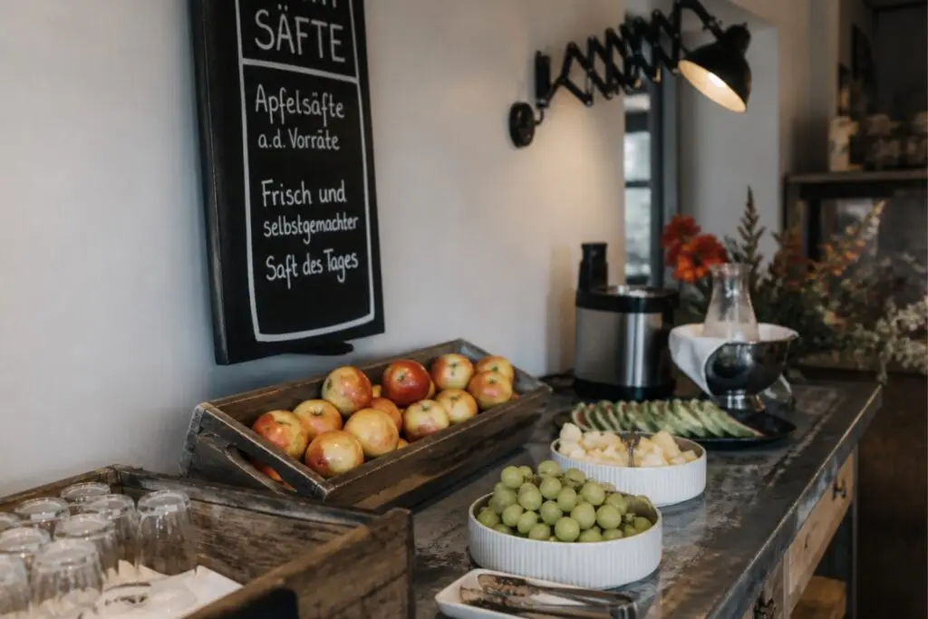 Frühstücksbuffet mit Äpfeln, Trauben, Melonen und einem Getränkeangebot in einem rustikalen, einladenden Ambiente.