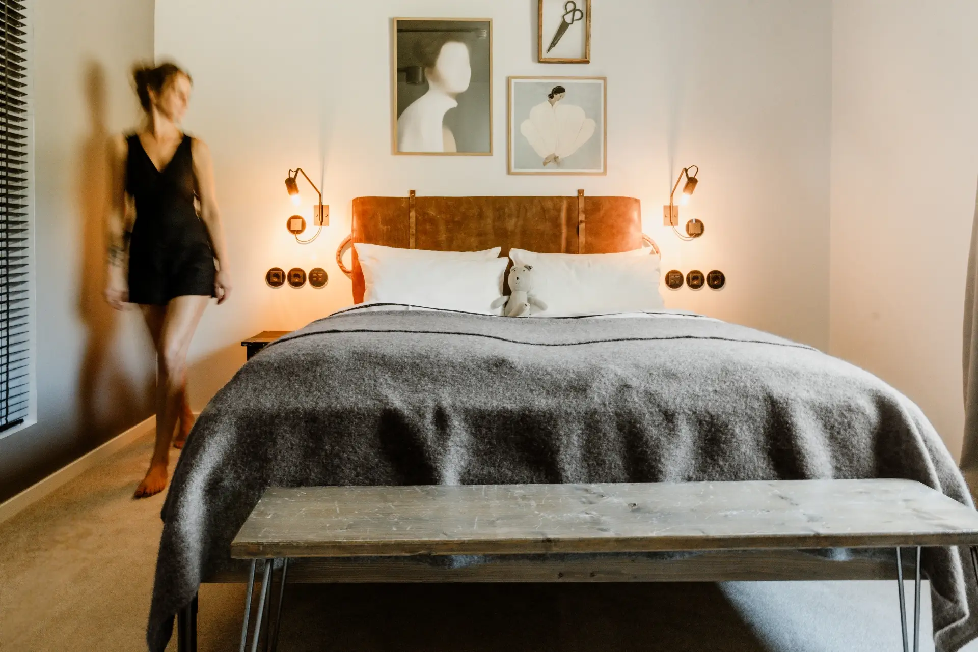 Eine Person in schwarzem Outfit bewegt sich durch ein modern eingerichtetes Schlafzimmer mit einem Bett und Kunst an der Wand.