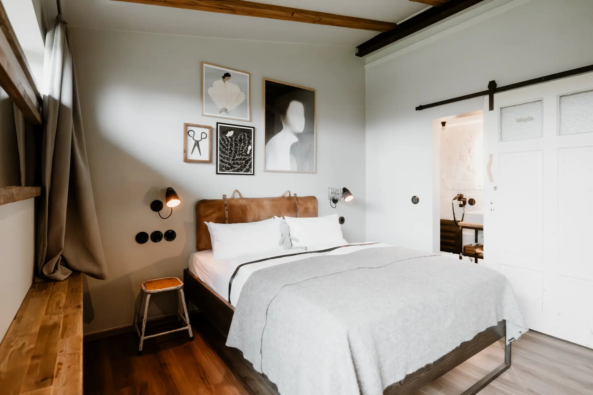 Modernes Schlafzimmer mit einem Doppelbett, Holzboden, Kunstwerken an der Wand und einer offenen Tür zu einem angrenzenden Raum.