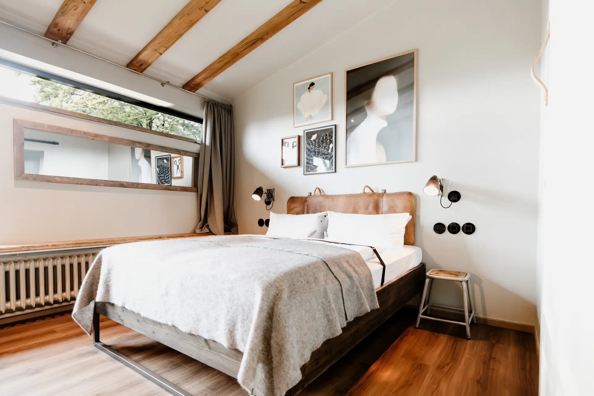 Modernes Schlafzimmer mit Bett, Bildern an der Wand und natürlichem Licht von einem Fenster, das auf Bäume blickt.