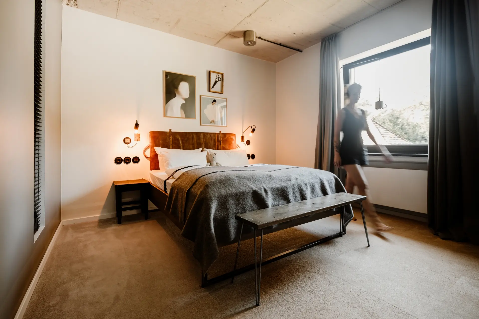 Modernes Schlafzimmer mit einem Bett, zeitgenössischen Bildern an der Wand und einer Person, die bewegt sich am Fenster vorbei.