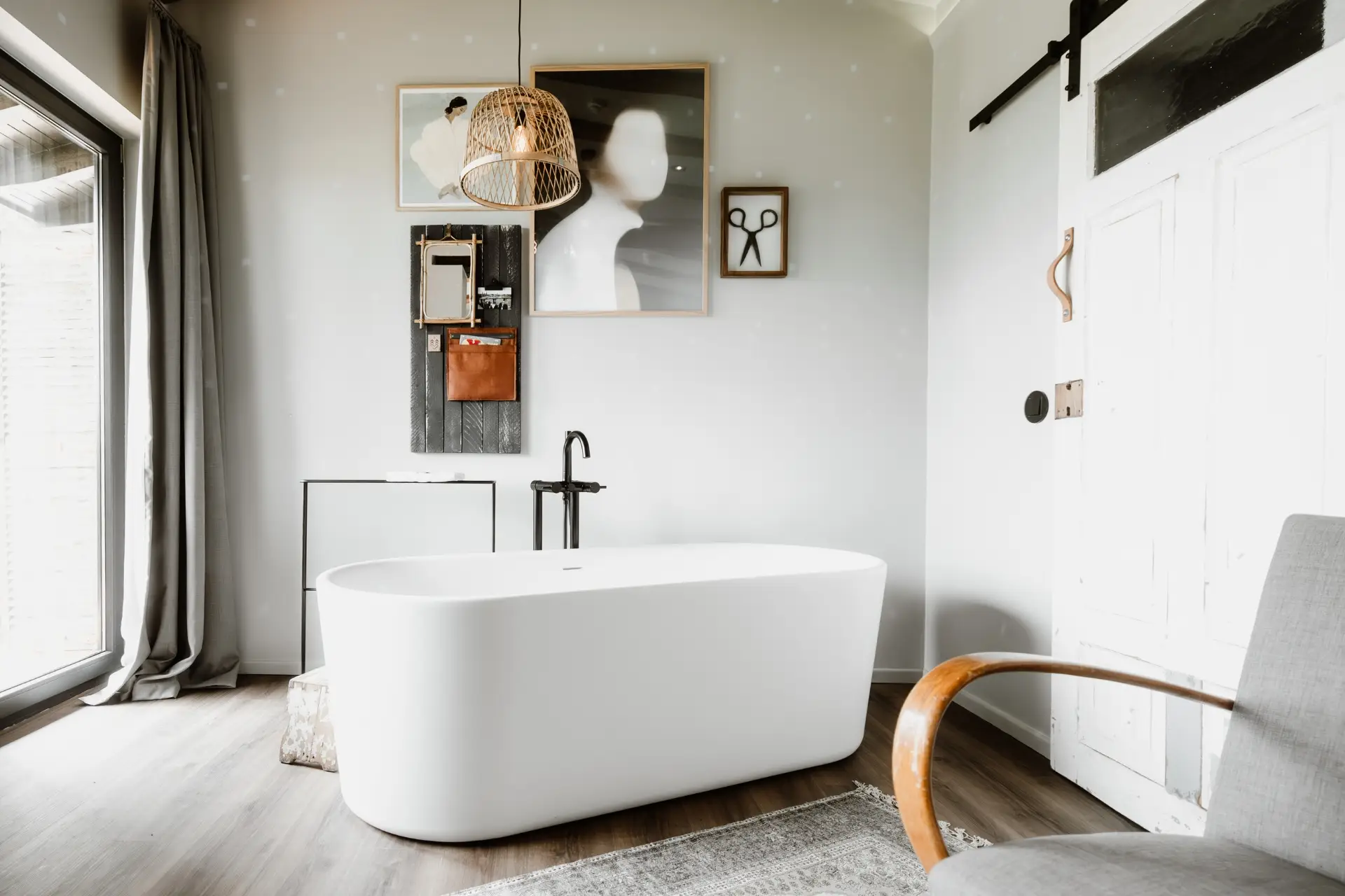 Modernes Badezimmer mit freistehender Badewanne, Holzdetails, Schreibtisch, Wandkunst und großen Fenstern.