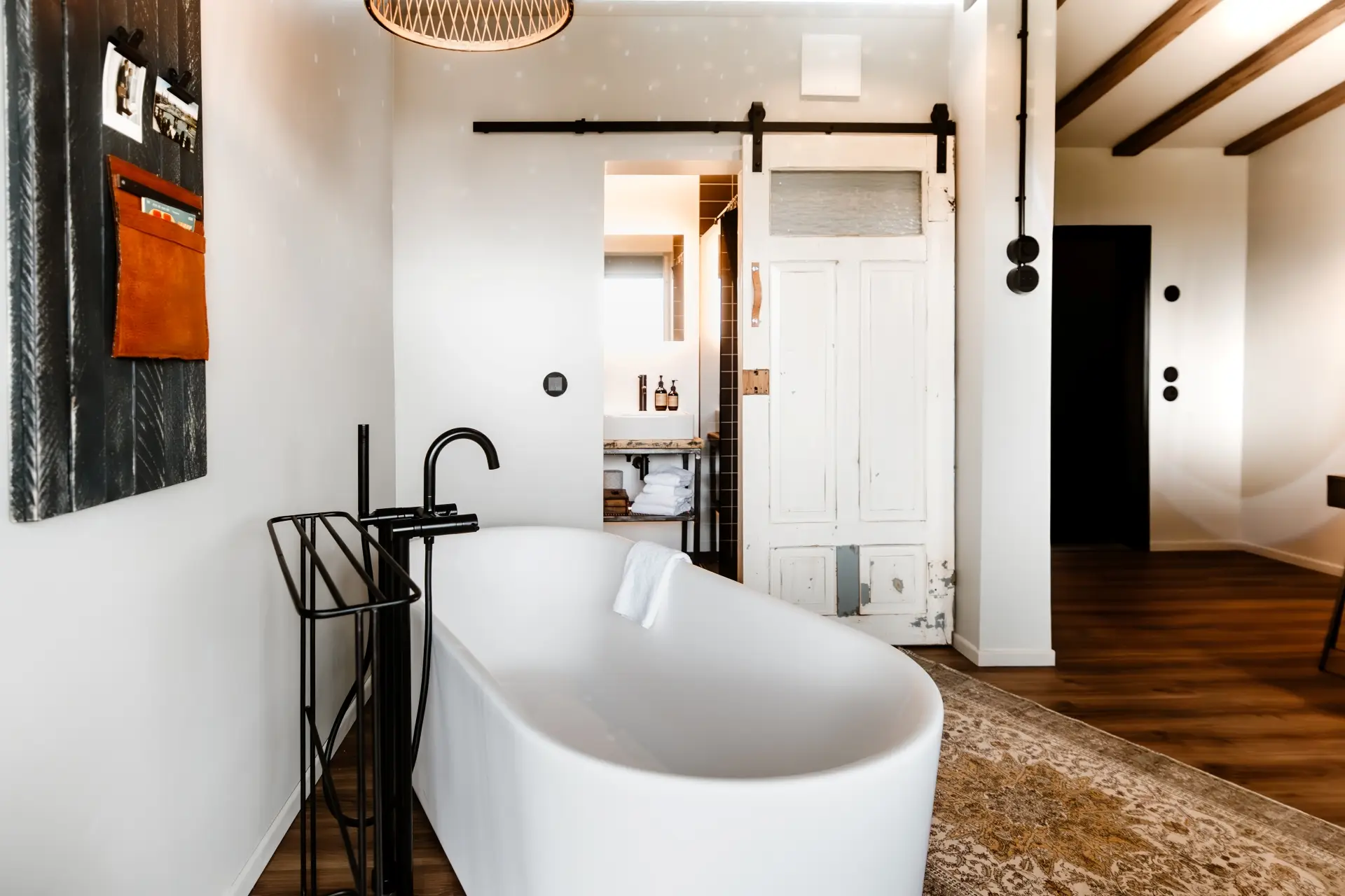 Modernes Badezimmer mit freistehender Badewanne, Holzdecke, schwarzer Armatur und einer alten Schiebetür im Hintergrund.