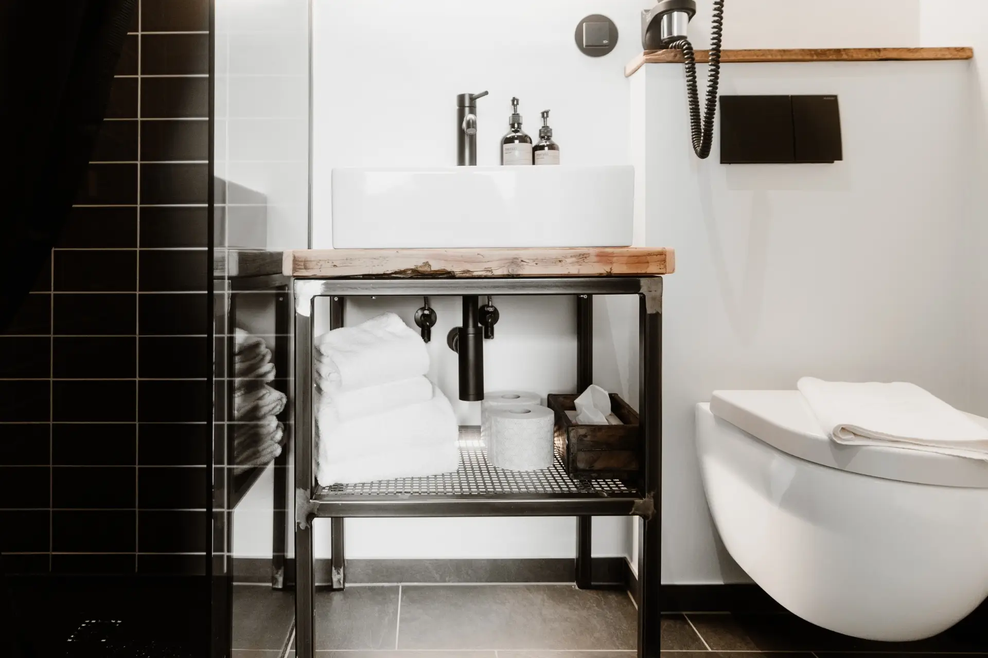 Moderne Badezimmeransicht mit Waschbecken auf einem Holzregal, Handtüchern, Toilettenpapier und Waschtisch.