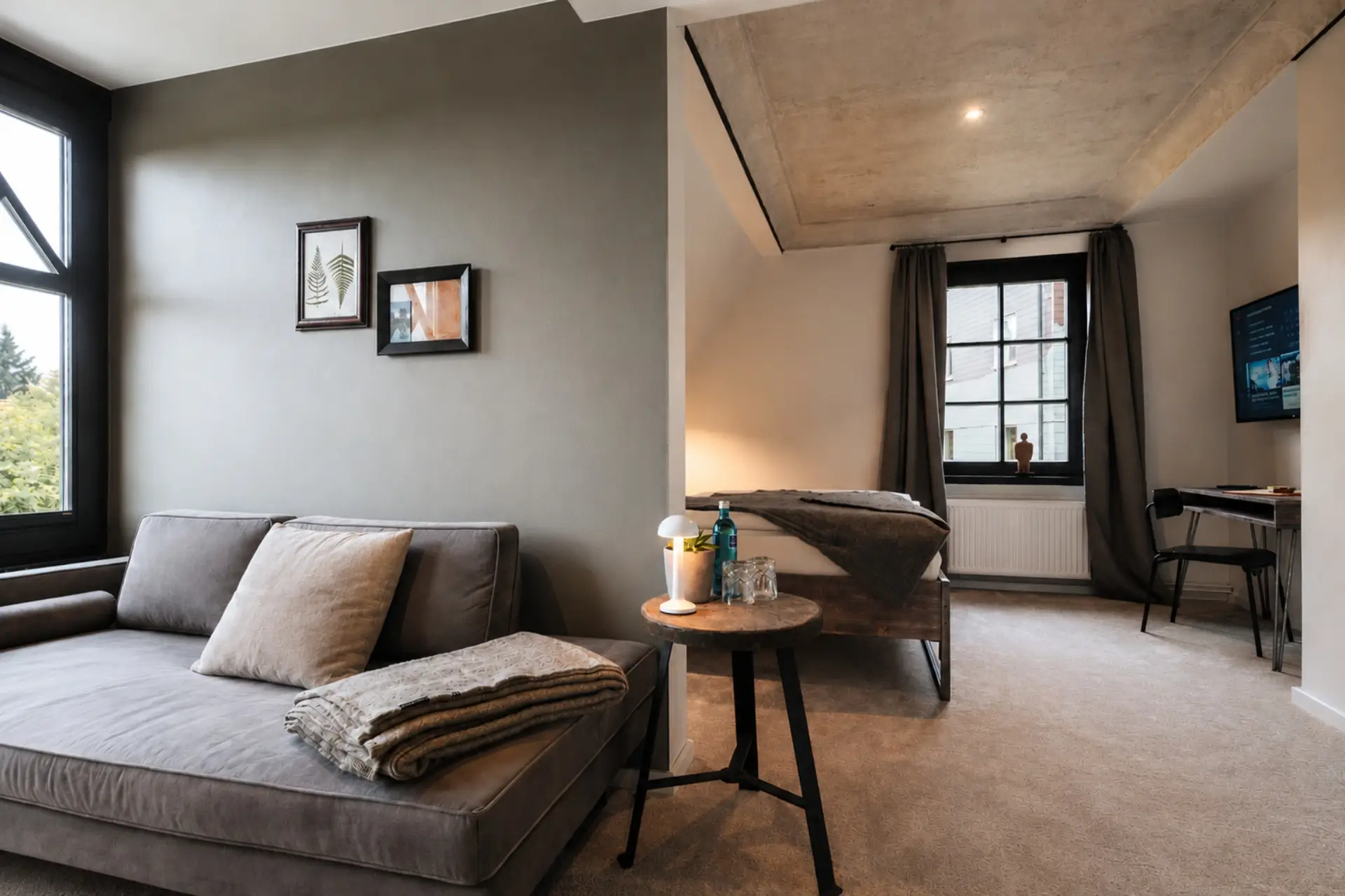 Gemütliches Zimmer mit Sofa, Tischlampe und Bett. Fenster mit Vorhängen, Bilder an der Wand und Schreibtisch.