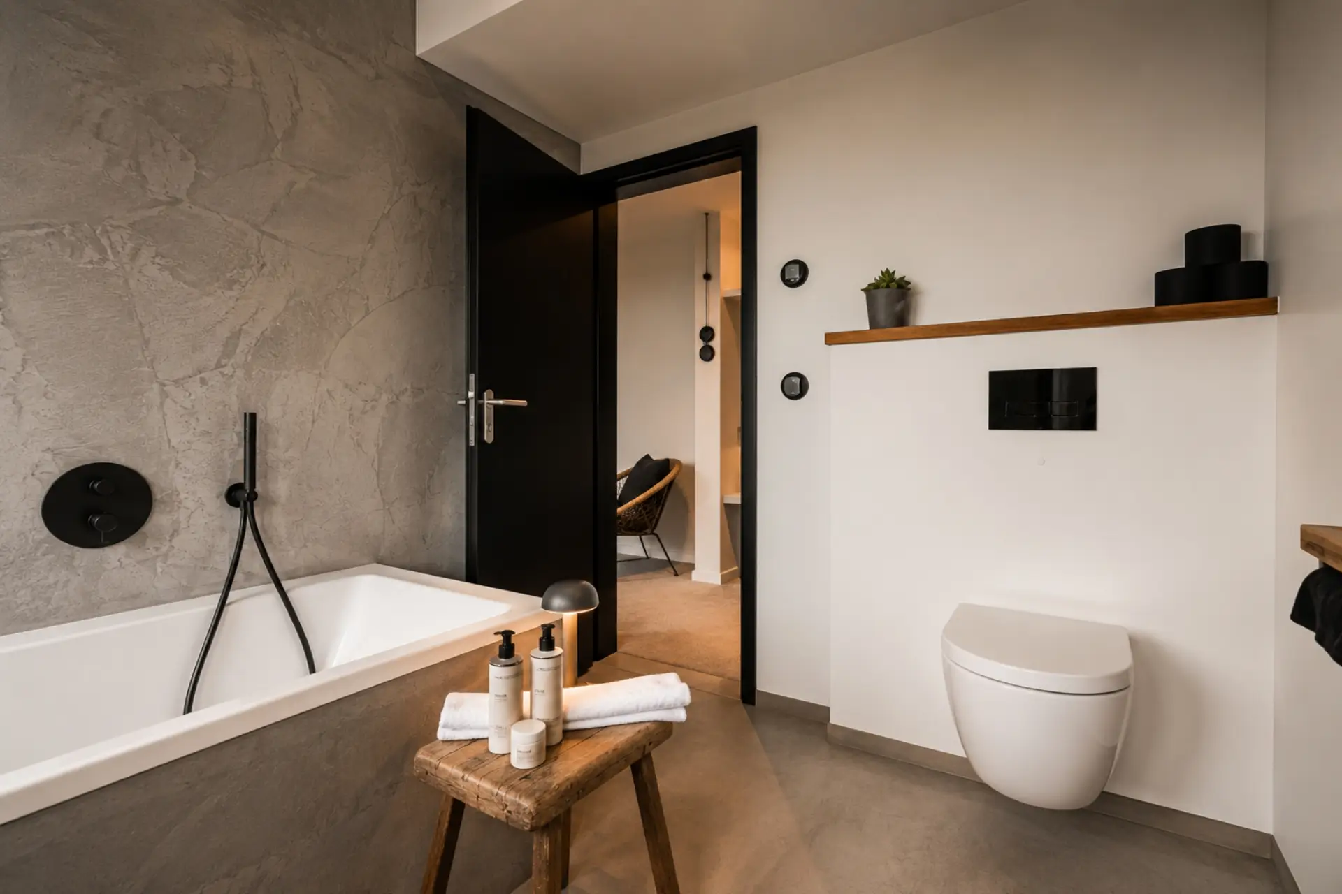 Bad mit freistehender Badewanne, modernen Armaturen und minimalistischem Design. Holzregal mit Pflegeprodukten und Pflanze.