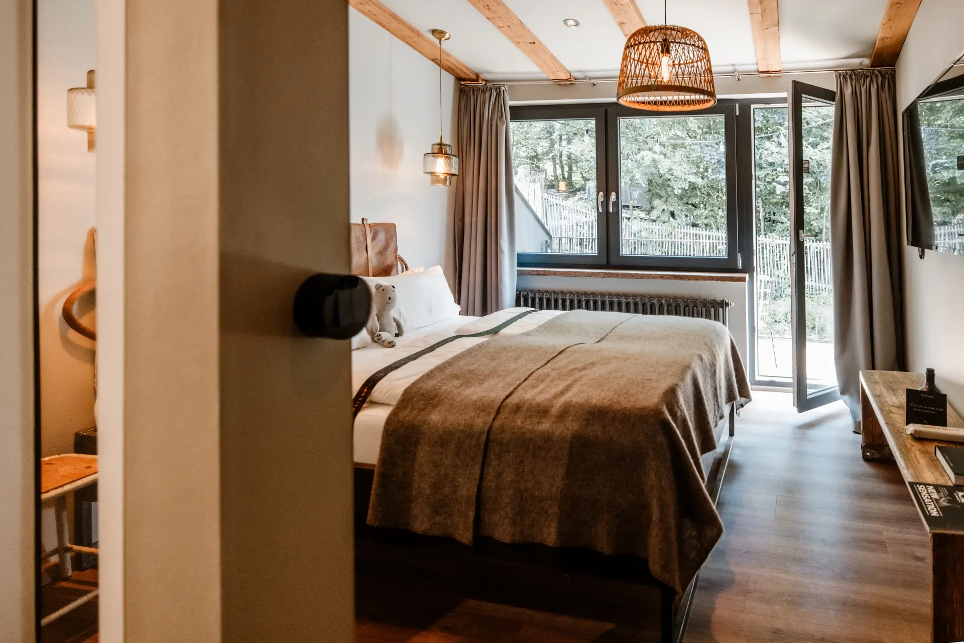 Blick in ein modernes Schlafzimmer mit einem Doppelbett, Fenster mit Aussicht und Holzbalken an der Decke.