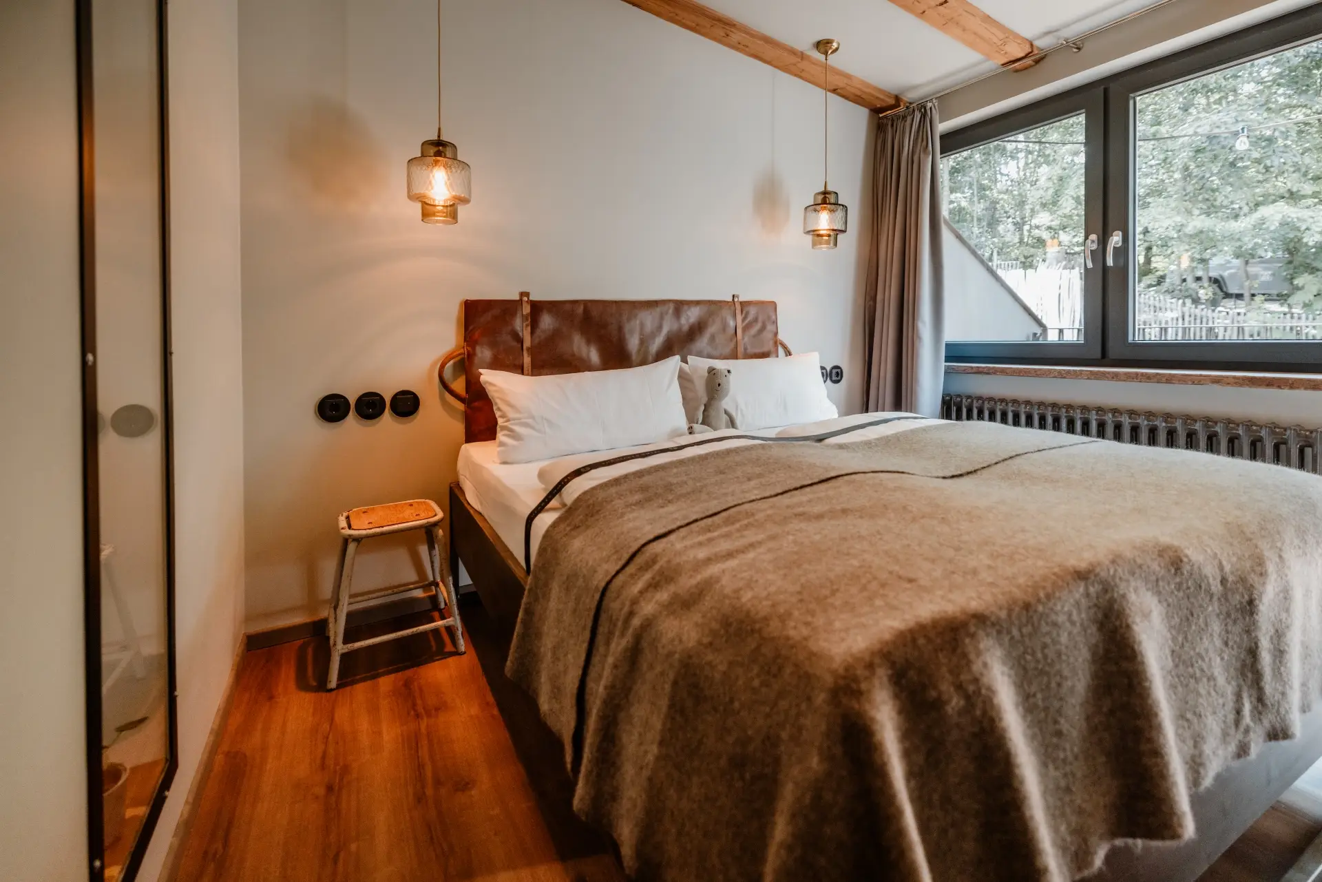 Modernes Schlafzimmer mit Doppelbett, Holzverkleidung, Laternenleuchten und Fensterblick auf Bäume draußen.