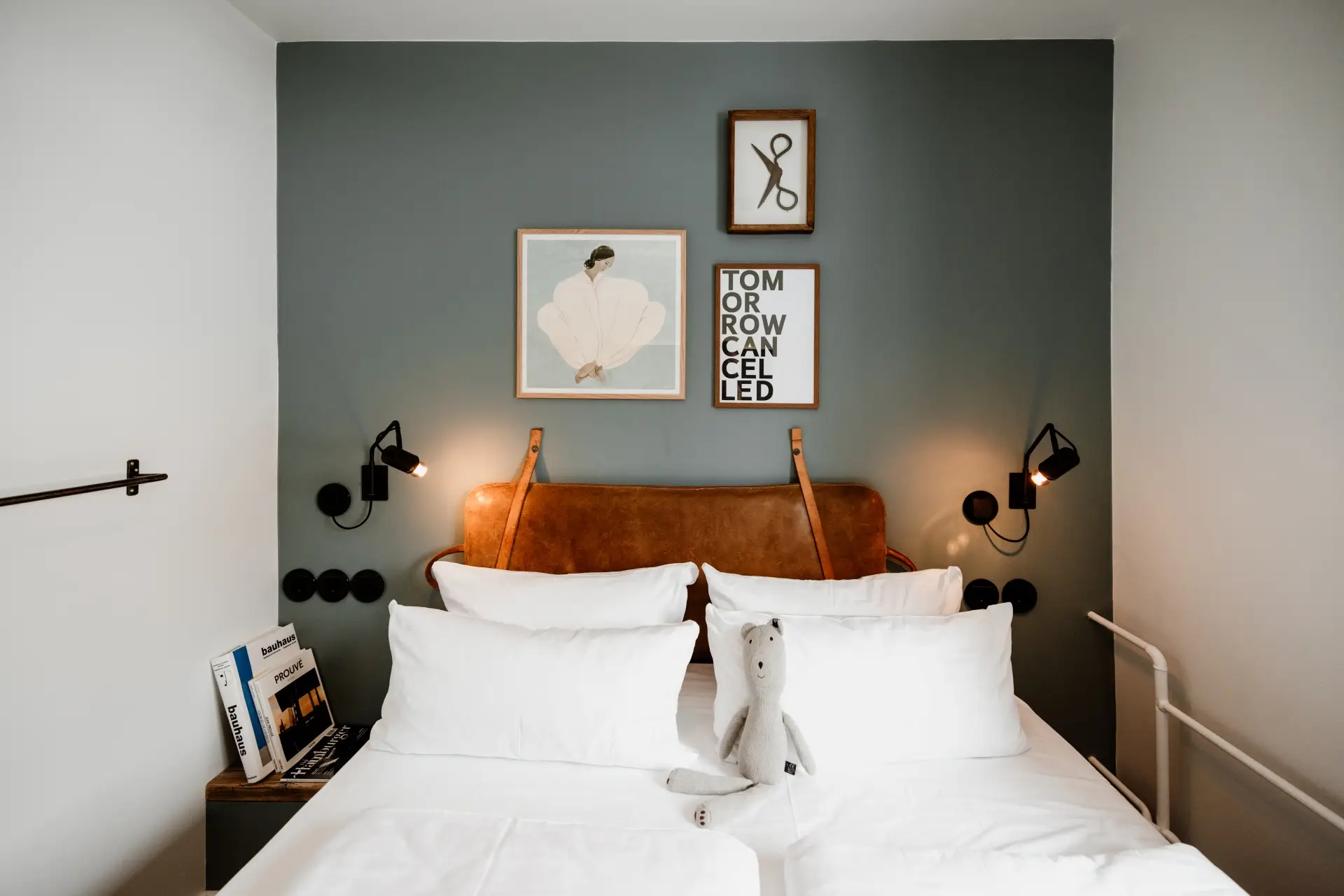 Modernes Zimmer mit einem Doppelbett, Kunstwerken an der Wand und einem Stofftier auf der Bettdecke. Leseleuchten am Kopfende.