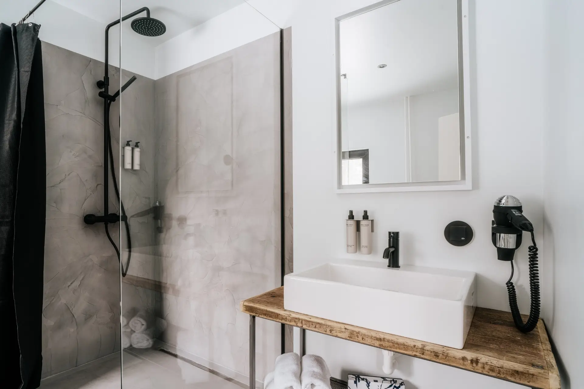 Modernes Badezimmer mit Dusche, Waschbecken, Spiegel und Fön. Elegante, minimalistische Ausstattung in hellem Design.