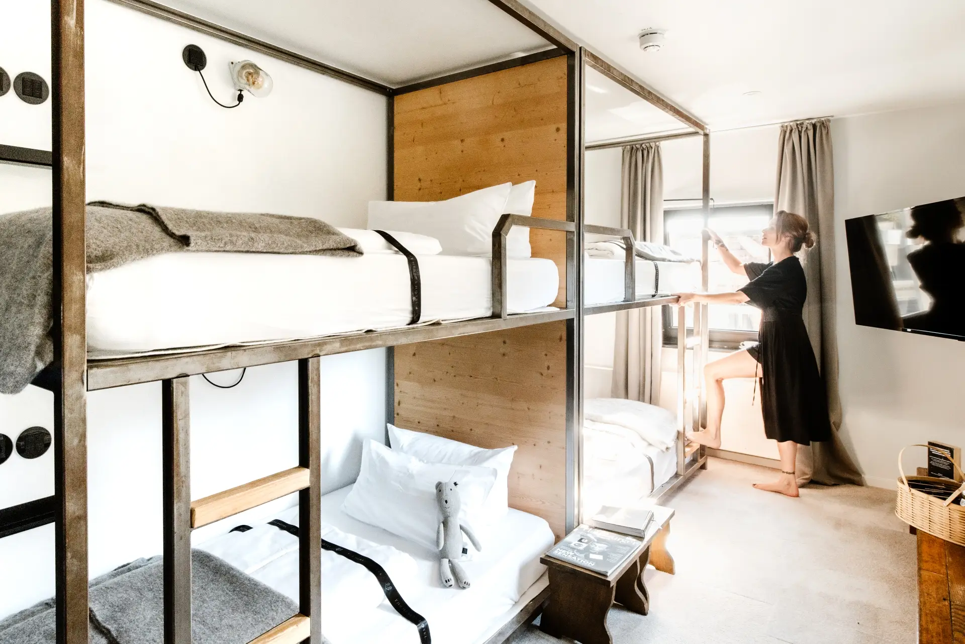 Frau in schwarzem Kleid steht an einem Etagenbett in einem modernen Gästezimmer und schaut aus dem Fenster.