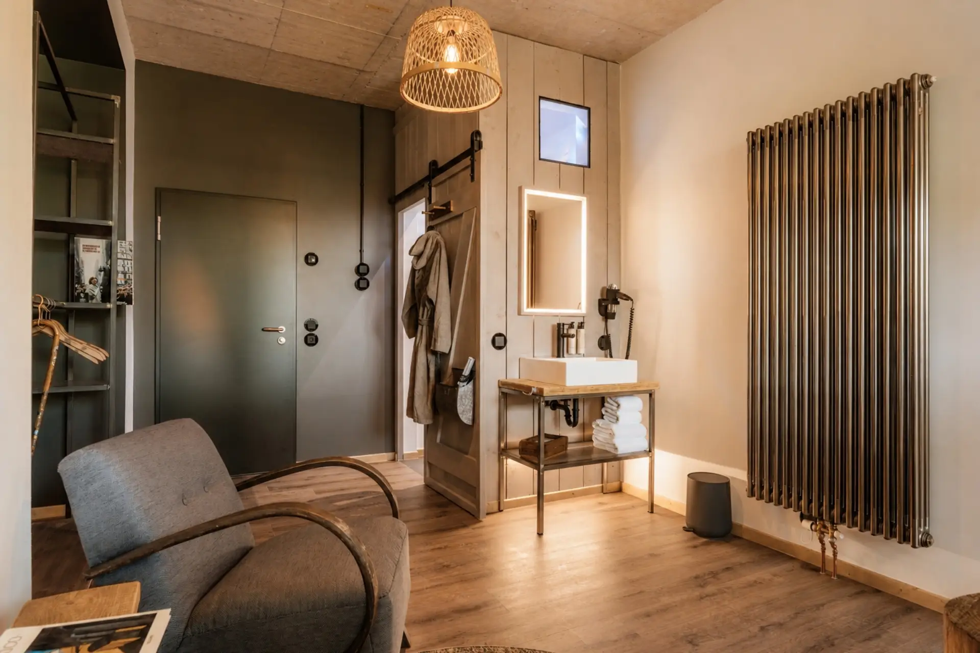 Modernes Badezimmer mit Holzregal, Waschbecken auf Holztisch, Handtüchern, einem Sessel und einem Heizkörper.