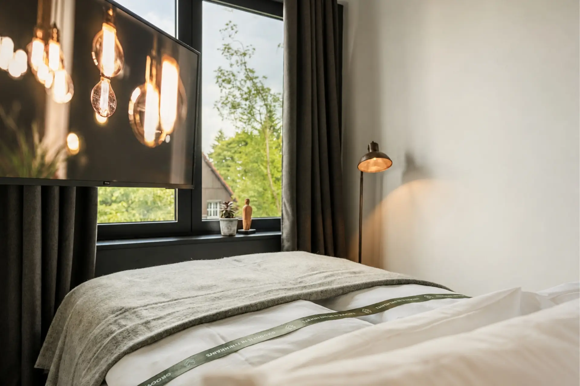 Ein modern eingerichtetes Schlafzimmer mit Betten, TV, Fensterblick und warmem Licht von einer Tischlampe.