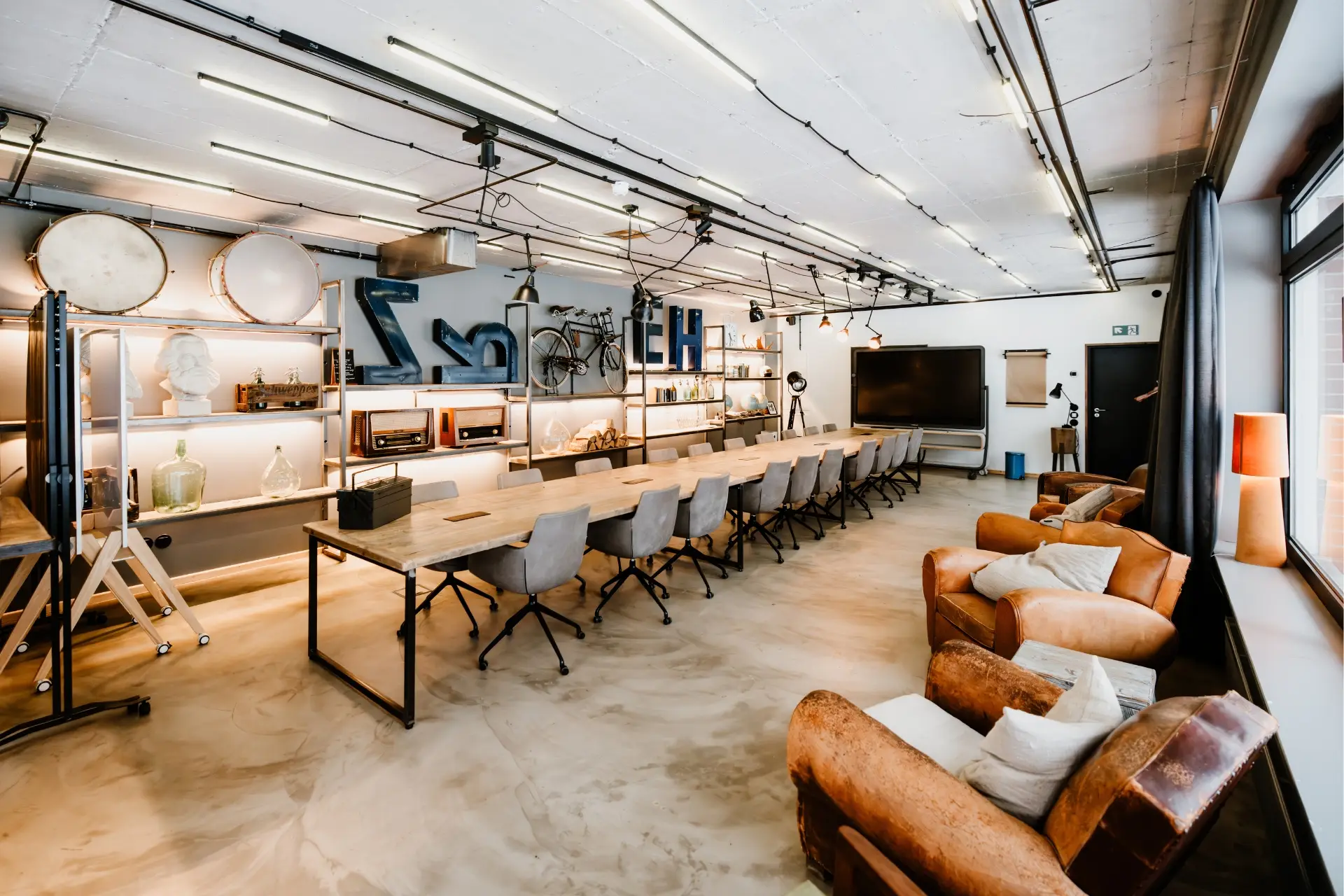 Stylischer Besprechungsraum mit langem Tisch, Designerstühlen, Regalen und moderner Technik an der Wand.