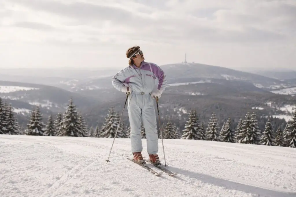 Person in Skiausrüstung steht auf einem schneebedeckten Hang, umgeben von Tannen, Blick in die Ferne auf eine Berglandschaft.
