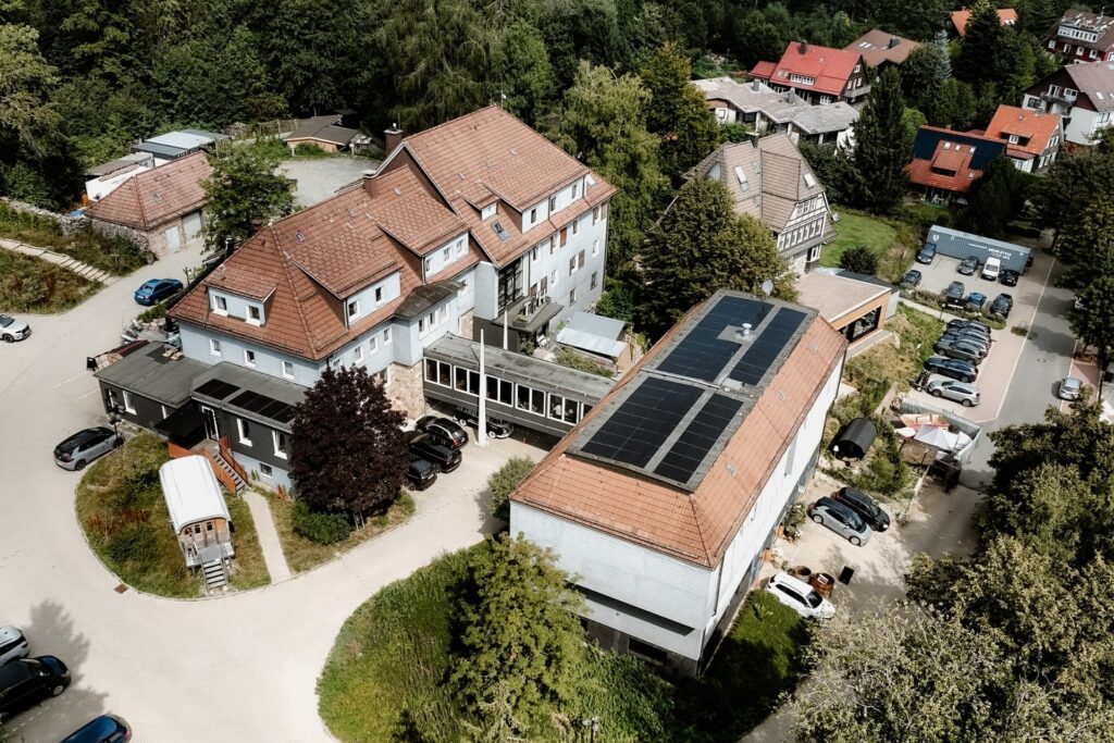 Luftaufnahme eines Gebäudekomplexes mit roten Dächern, Parkplätzen und Bäumen in einer ländlichen Umgebung.