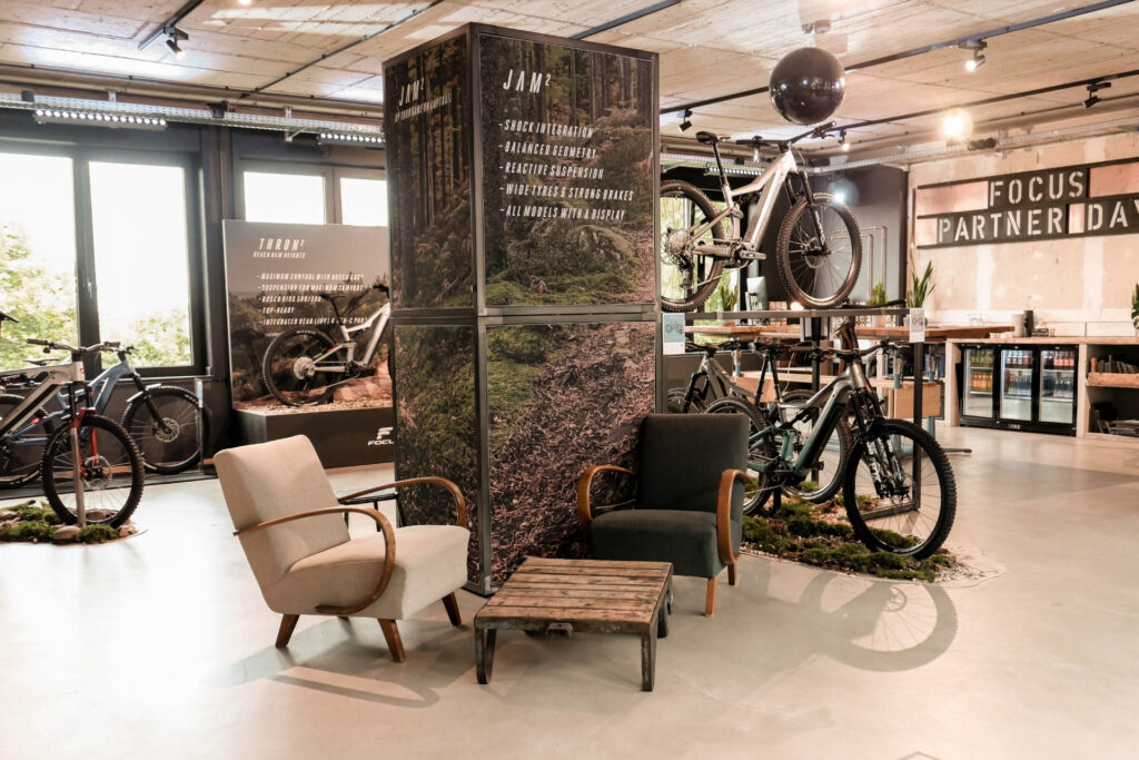 Moderne Fahrrad-Ausstellung mit Sitzgelegenheiten, Werbetafeln und verschiedenen Fahrrädern in einem hellen Raum.
