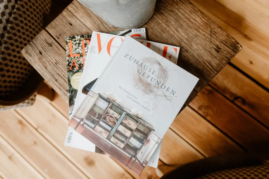 Stapel von drei Magazinen auf einem Holztisch, darunter „Zuhause gefunden“ und zwei weitere Titel. Holzoberfläche im Hintergrund.