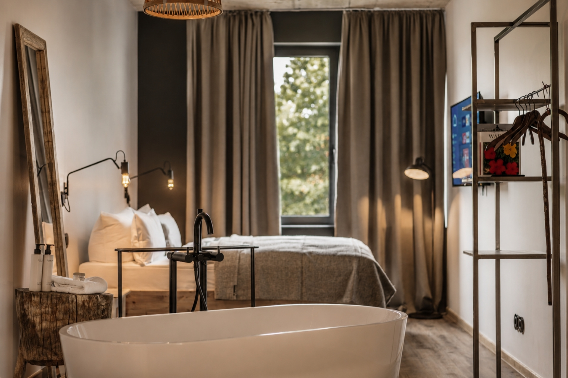 Hellbraunes, modernes Hotelzimmer mit einem Bett, freistehender Badewanne und TV, Tageslicht durch große Fenster.