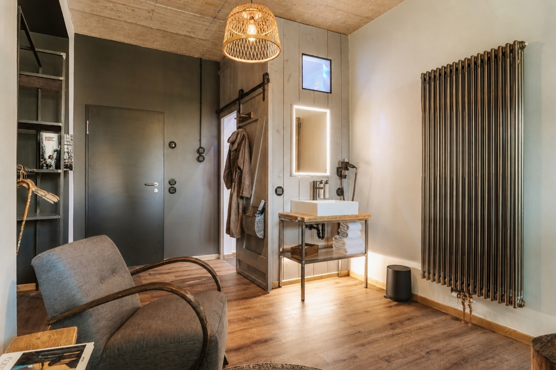 Moderne Wohnatmosphäre in einem Badezimmer mit Holzdetails, Handtuchablage, Waschbecken und einem bequemen Sessel.