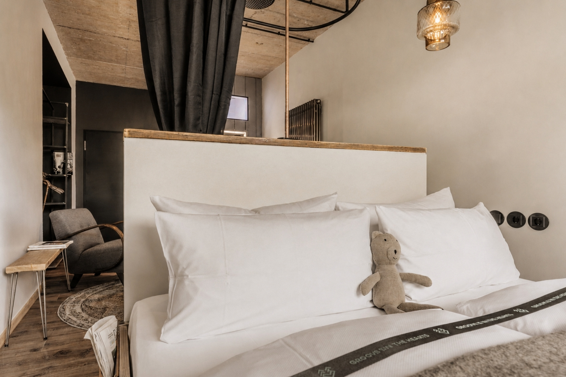 Gemütliches Schlafzimmer mit großen, weißen Kissen, einem Stofftier und einem modernen Sessel in einem stilvollen Raum.