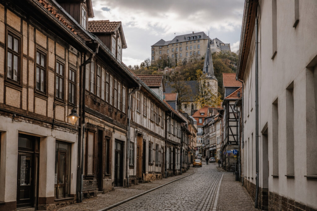 Alt-Text: Blick auf eine schmale, gepflasterte Straße mit historischen Fachwerkhäusern und einer Kirche im Hintergrund.
