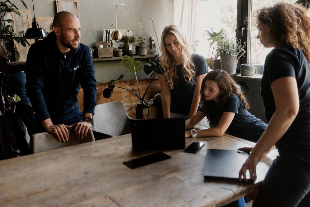 Vier Personen in einem modernen Büro besprechen konzentriert an einem Tisch die Inhalte eines Laptops.