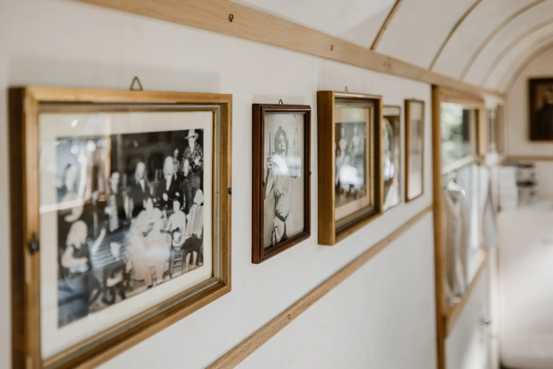 Wand mit gerahmten Schwarz-Weiß-Fotos von Personen bei einer Veranstaltung in einem hellen, modernen Innenraum.