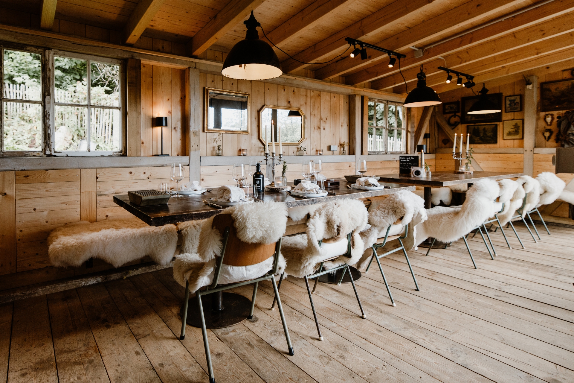 Rustikaler Essbereich mit Holztisch, Stühlen mit Fellüberzügen, Kerzen und eleganter Tischdekoration in einem gemütlichen Holzraum.
