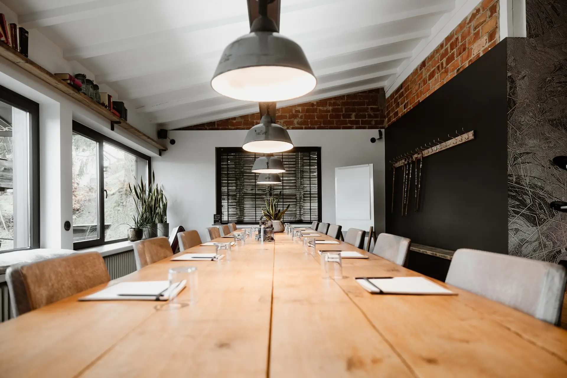 Konferenzraum mit einem langen Holztisch, Stühlen, Schreibblock und Gläsern, beleuchtet von modernen Deckenleuchten.